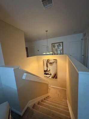 A staircase with a beige carpet, a wall-mounted artwork, and a pendant light.