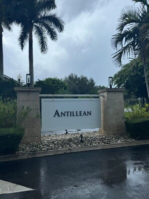A sign with the name 'ANTILLEAN' on a building entrance, surrounded by greenery and palm trees.