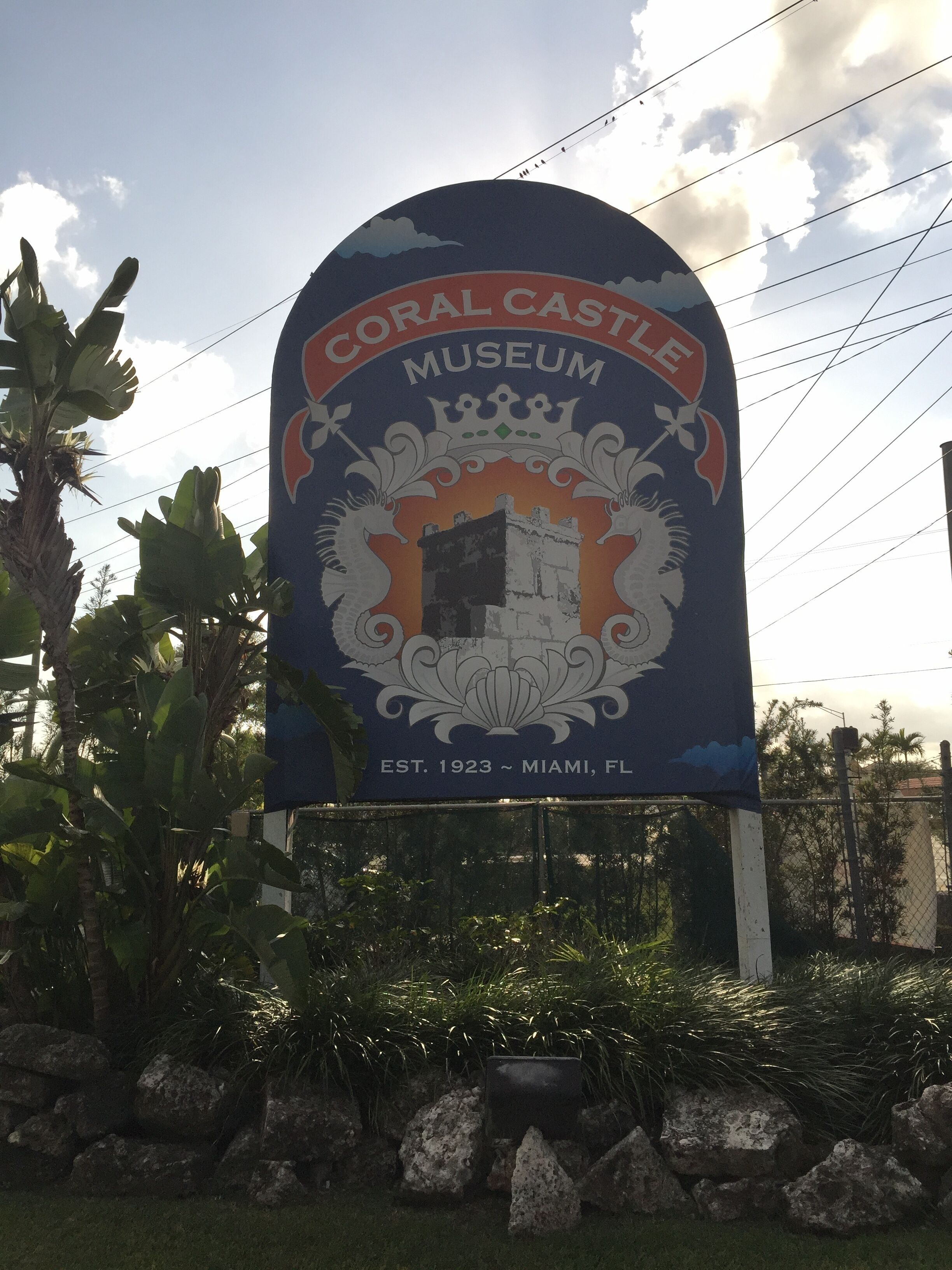 A sign for the Coral Castle Museum with a castle emblem, established in 1923, located in Miami, FL.