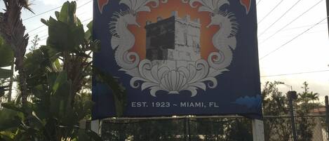 A sign for the Coral Castle Museum with a castle emblem, established in 1923, located in Miami, FL.