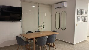 Een moderne vergaderruimte met een houten tafel, zes stoelen, een flatscreen televisie, een glazen scheidingswand, twee spiegelwanden en een airconditioner.