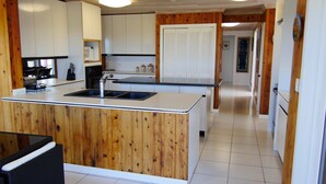 A kitchen with wooden cabinets, a sink, and a countertop. There is a dining area with a table and chairs. The kitchen has a white tiled floor and wooden walls. - Las Breezes 5 Bedroom Villa, With 1/2 Mile Private Beach On Hooper's Bay (George Town)