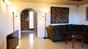 A living room with a sofa, a coffee table, and two floor lamps. There is a door leading to another room and a wall with a patterned design. - Las Breezes 5 Bedroom Villa, With 1/2 Mile Private Beach On Hooper's Bay (George Town)