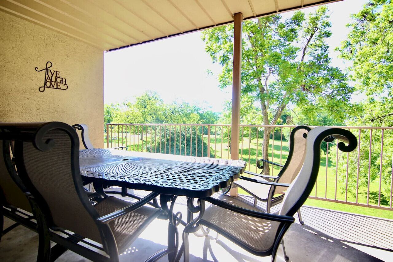 Een overdekt terras buiten met een tafel en stoelen, een decoratief bord en uitzicht op een groen landschap.