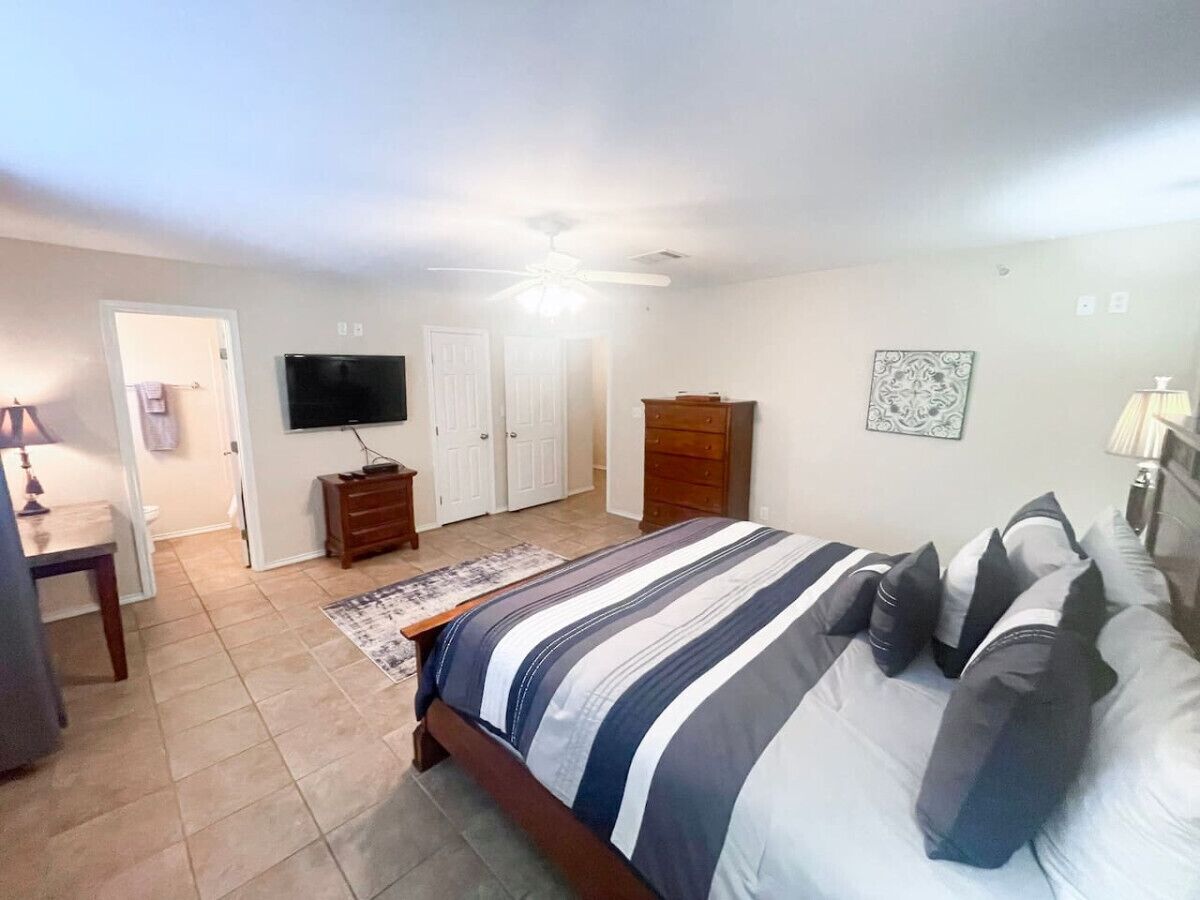 Een slaapkamer met een bed, televisie, dressoir en plafondventilator.