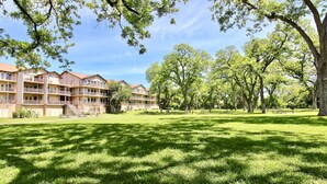 A courtyard with a grassy lawn, trees, and a building with multiple balconies and windows. - 2 Night MIN Only MDW | 2 Pools/4 Hot Tubs (New Braunfels)