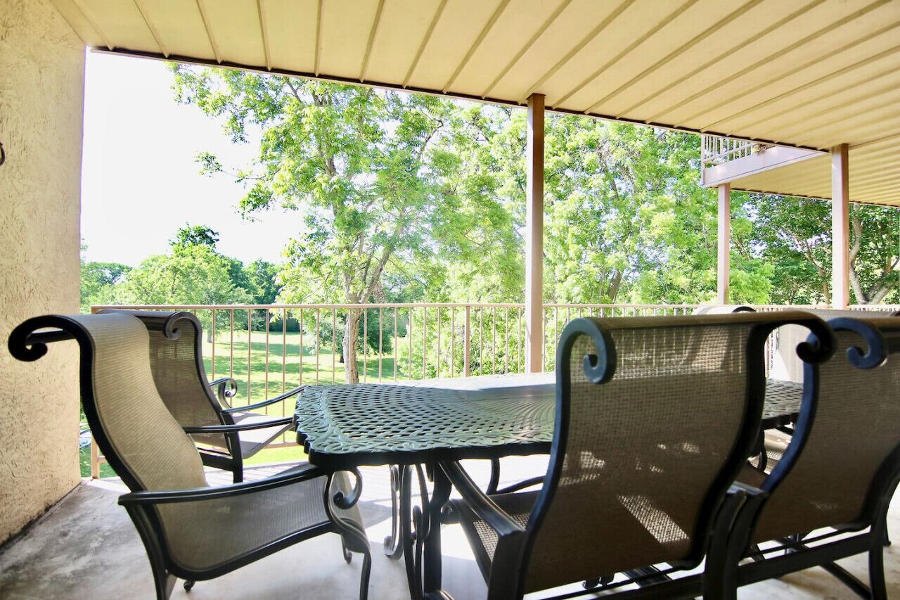 An outdoor patio with a table and chairs, a covered area, and a view of trees and a fence.