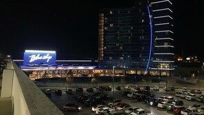 En parkeringsplats med flera bilar, ett hotell med en tydlig skylt som visar namnet ”B Hotel”, och en modern byggnad med upplysta linjer.