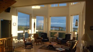 A spacious living room with large windows, a fireplace, and a variety of seating options. - Island House Above Trees! 360° Oceanview, 4BR, Car-Accessible, Near Lunenburg   (La Have Island)