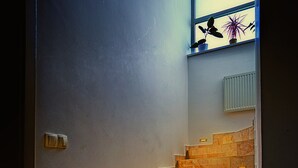 A staircase with marble steps leading to a landing area with a radiator and a window with plants. - Gorgeous quiet large townhouse on Budapest border (Budaörs)
