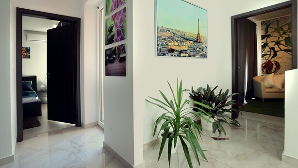 A modern hallway with a cityscape painting, potted plants, and a glimpse of a bedroom with a bed and a nightstand. - Gorgeous quiet large townhouse on Budapest border (Budaörs)