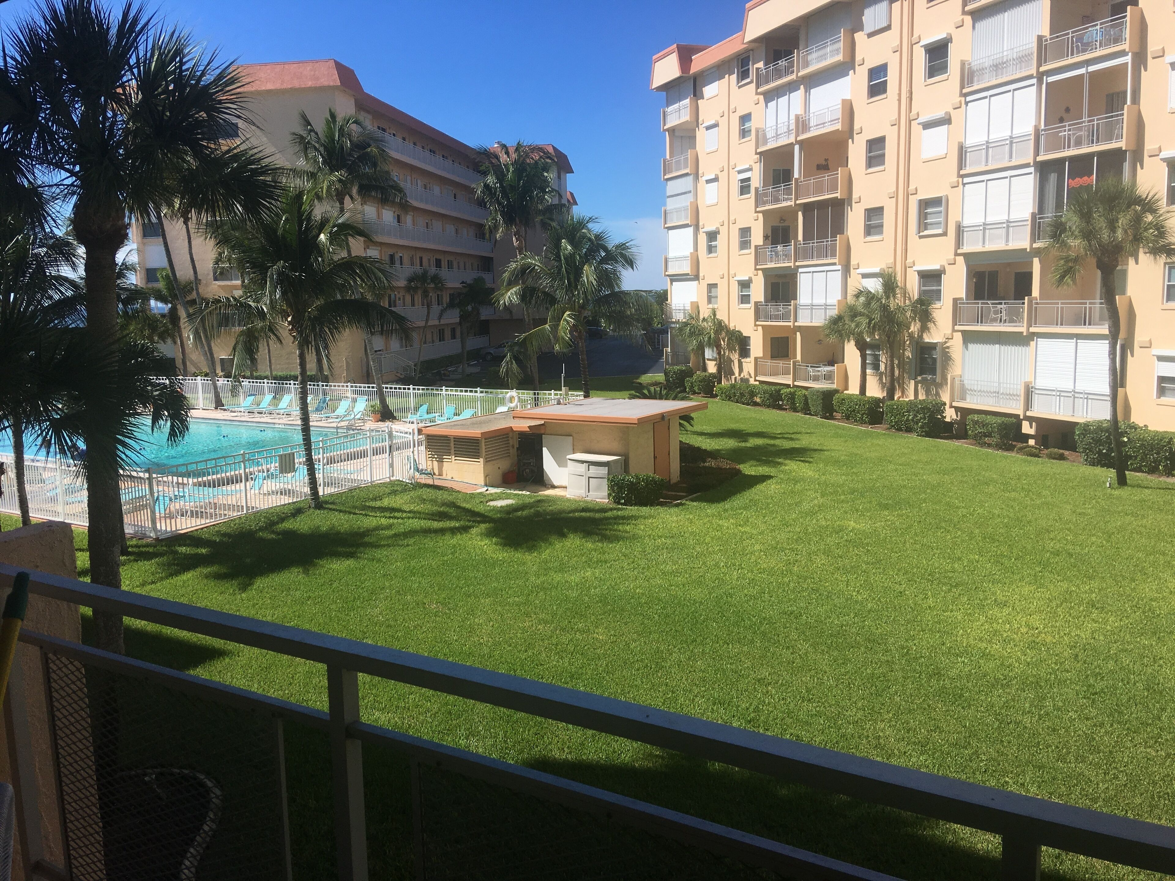 Une cour d’hôtel avec une piscine, des palmiers et un petit bâtiment.