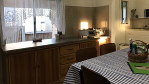 Une cuisine équipée d’une cuisinière, d’une fenêtre ornée de rideaux en dentelle, de meubles de rangement en bois et d’une table recouverte d’une nappe à rayures.