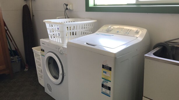 Un lave-linge à chargement frontal, surmonté d’un sèche-linge également à chargement frontal, un panier à linge blanc et un évier utilitaire.