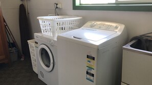 A front-loading washing machine with a front-loading dryer stacked on top, a white laundry basket, and a utility sink.