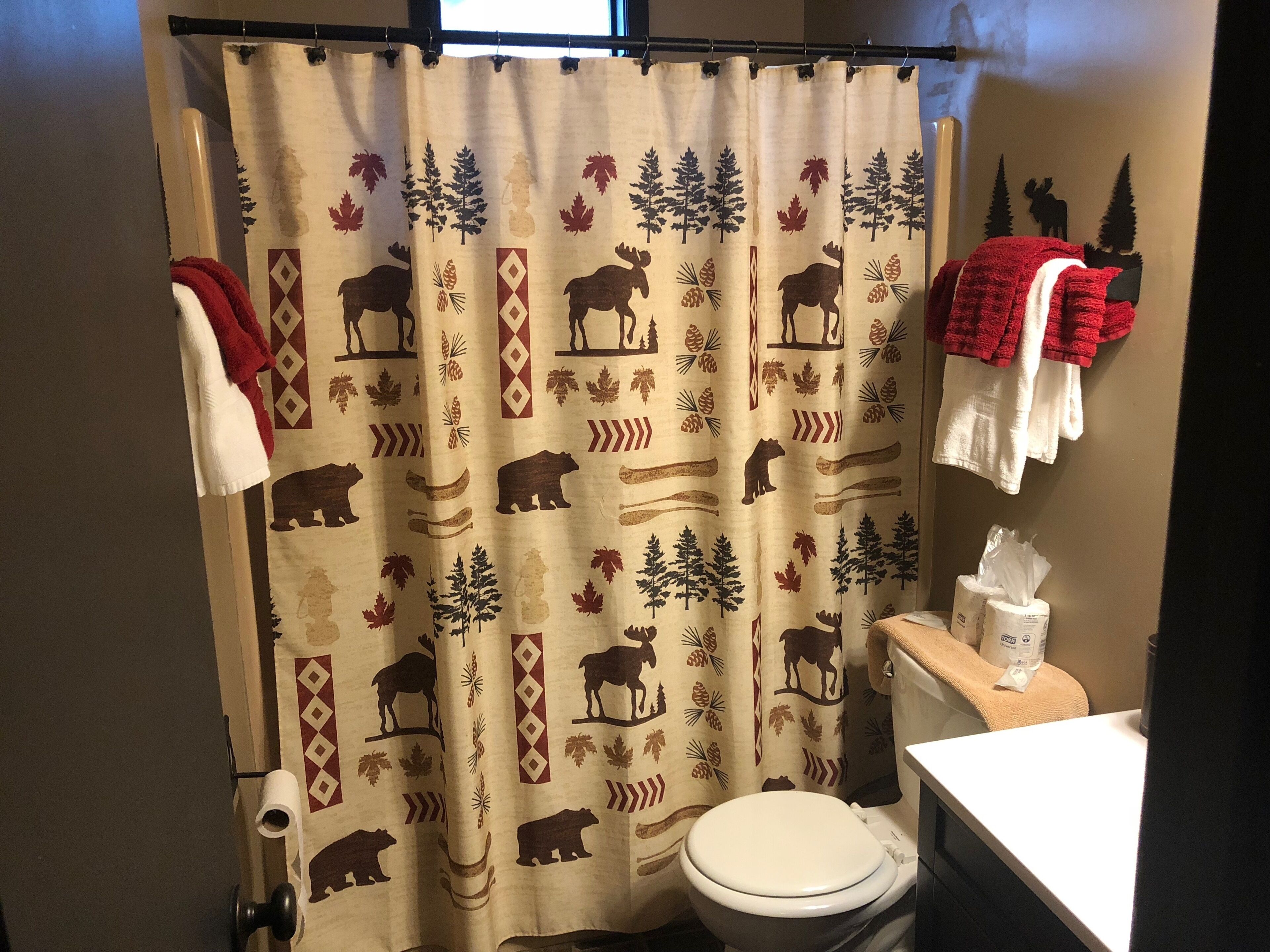 A bathroom with a shower curtain featuring a nature-themed print, a toilet, a towel rack with towels, and a tissue box on the counter.