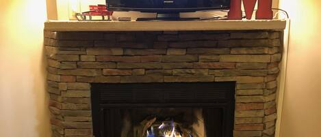 A fireplace with a television above it, a red 'M' decoration, and two wall-mounted lanterns.