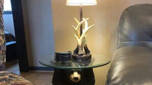 Una habitación con una lámpara de mesa de vidrio, una mesa con forma de oso, un sofá estampado y una silla de cuero.