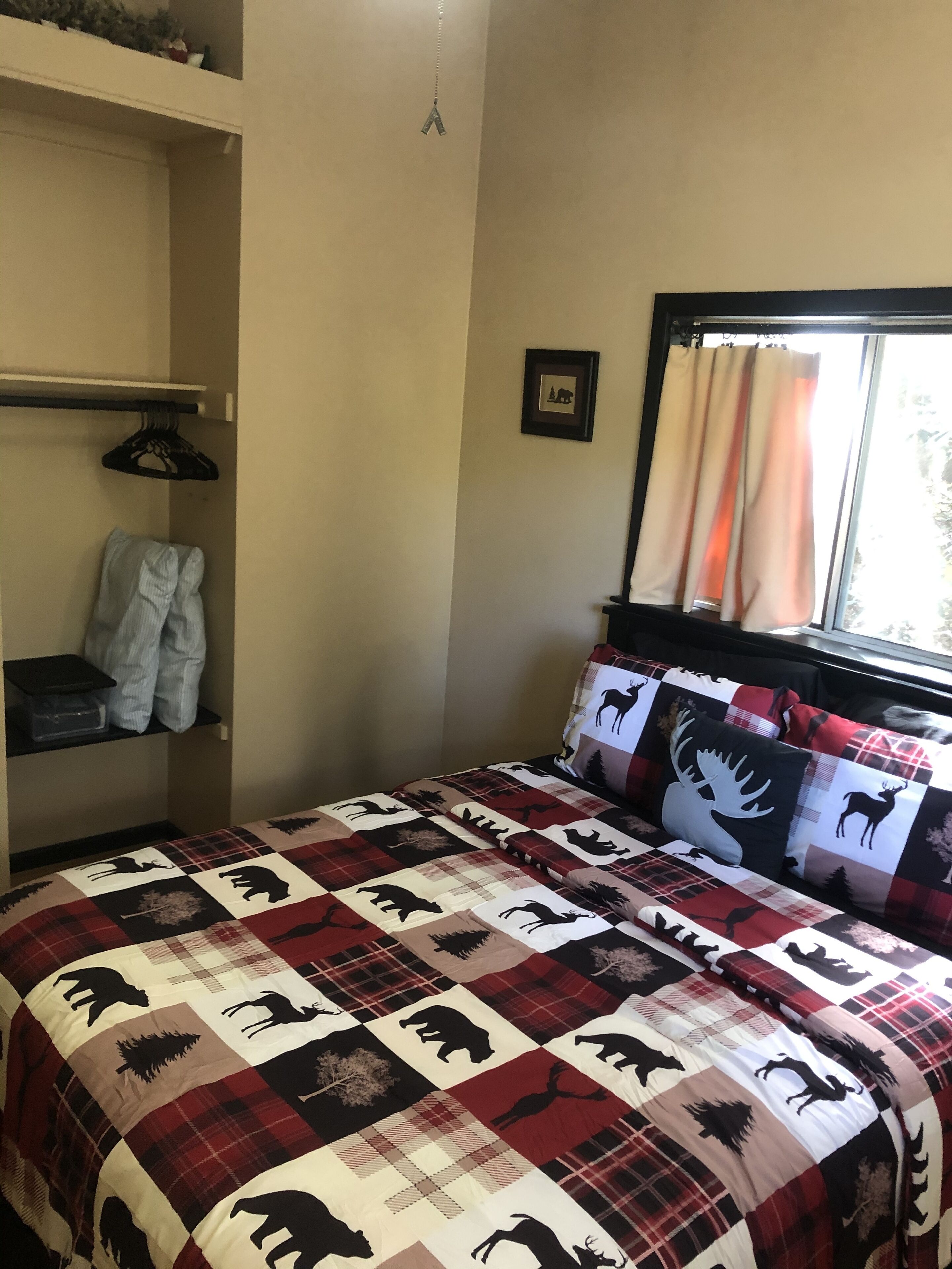 Un dormitorio con una colcha escocesa con estampados de animales, una ventana con cortinas, un perchero y un cuadro en la pared.