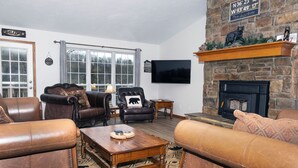Una sala de estar con sofás de cuero, una mesa de centro de madera, una chimenea de piedra y un televisor montado en la pared.