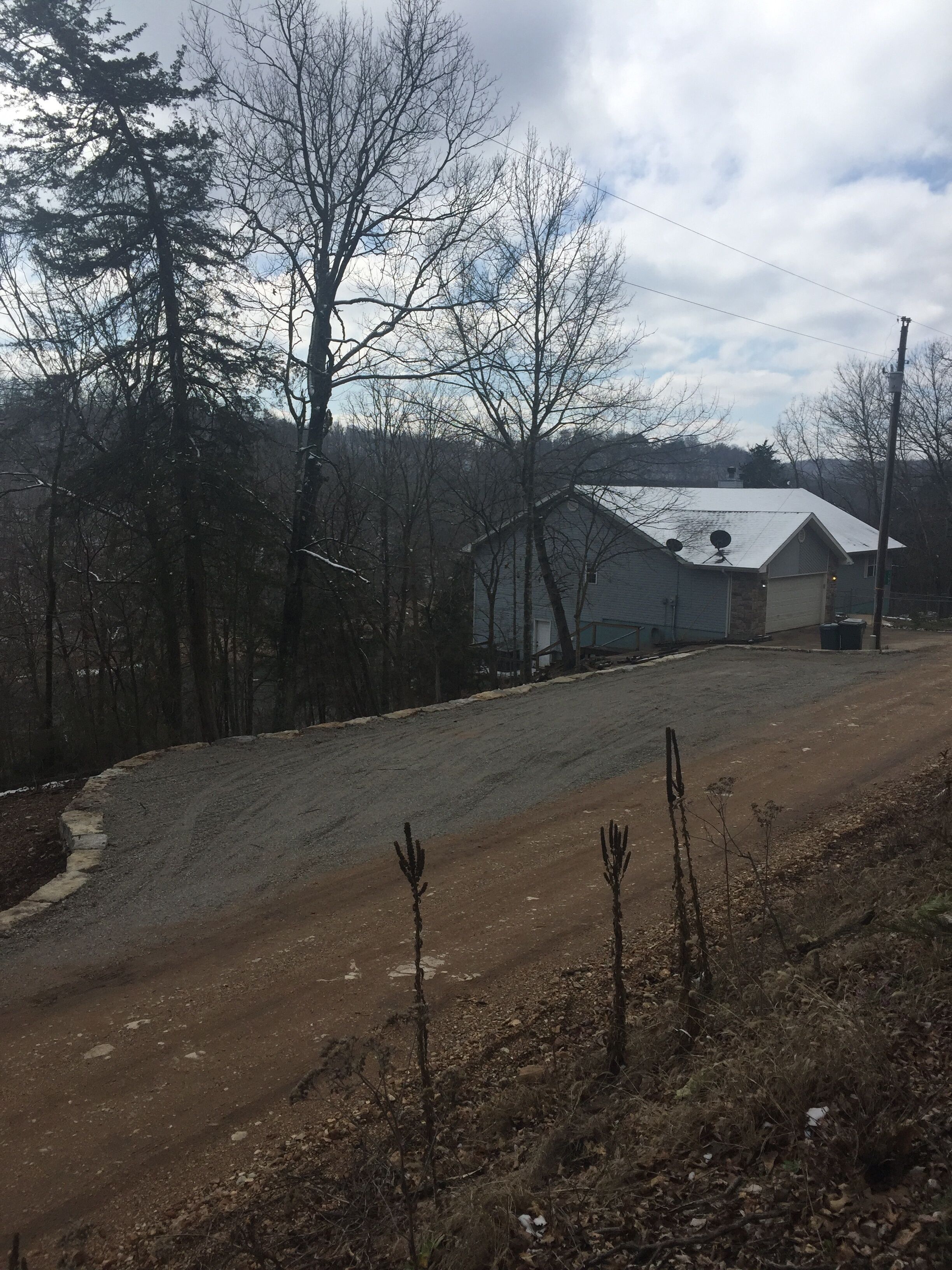 Une route de campagne avec un chemin de terre menant à une maison dotée d’un toit en métal et d’une antenne parabolique.