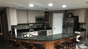 A modern kitchen with a central island, bar stools, stainless steel appliances, and wooden cabinetry. - Bayou Life Lodging, Charter Fishing, Ecotourism. Only 25 miles to French Quarter (Barataria)
