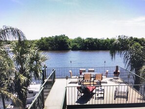 Relax on the deck overlooking the serene water, surrounded by lush greenery and comfortable lounge seating.
