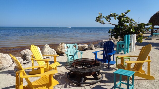 A beach setting with several Adirondack chairs, a fire pit, and a view of the ocean. - Oceanfront Property in Kawama Tower with Elevator, Lagoon and 2 Heated Pools (Key Largo)