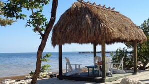 A beachside hut with a thatched roof, white chairs, and a table. - Oceanfront Property in Kawama Tower with Elevator, Lagoon and 2 Heated Pools (Key Largo)