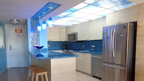 A modern kitchen with a central island, stainless steel appliances, and blue-tiled backsplash. - Oceanfront Property in Kawama Tower with Elevator, Lagoon and 2 Heated Pools (Key Largo)