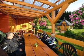 A covered outdoor dining area with a wooden table and chairs, surrounded by a wooden pergola.