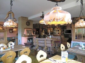 Un comedor rústico con mesas y sillas de madera, lámparas colgantes y una barra al fondo.