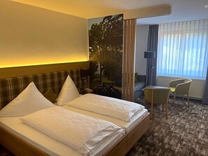 A hotel room with a bed, a desk, a chair, and a large window with curtains.