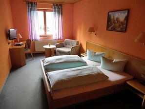 A hotel room with a bed, a desk, a chair, a small table, and a window with curtains.