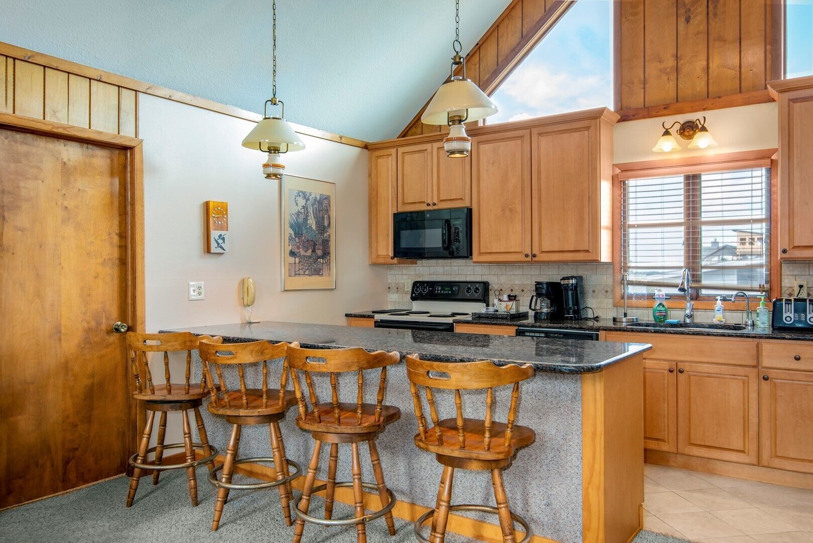 A kitchen with wooden cabinets, a central island with bar stools, a microwave, and a coffee maker.