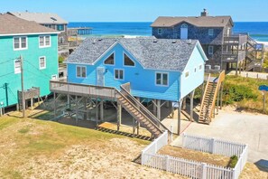 A coastal house with a wooden deck and stairs leading to a beach.