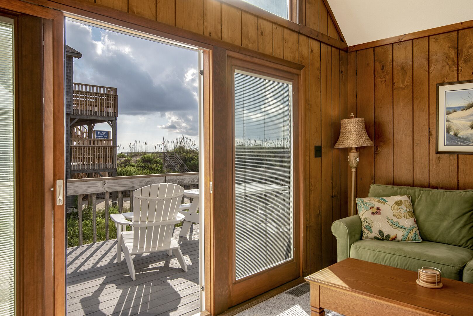 A wooden interior with a sliding glass door leading to a deck, a green sofa, and a lamp.