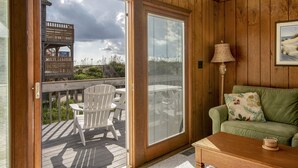 Un interior de madera con un gran ventanal corredero que da a una terraza, un sofá verde y una lámpara.