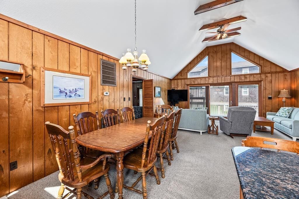 A wooden interior with a dining table, chairs, a TV, and a sofa.