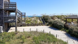 Un edificio frente a la playa con una terraza de madera y una escalera que baja a la arena.