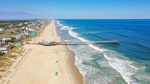 A beach with a pier extending into the ocean, surrounded by residential buildings. - 414 Semi-Ocean Front -Walking Distance to Pier! (Nags Head)