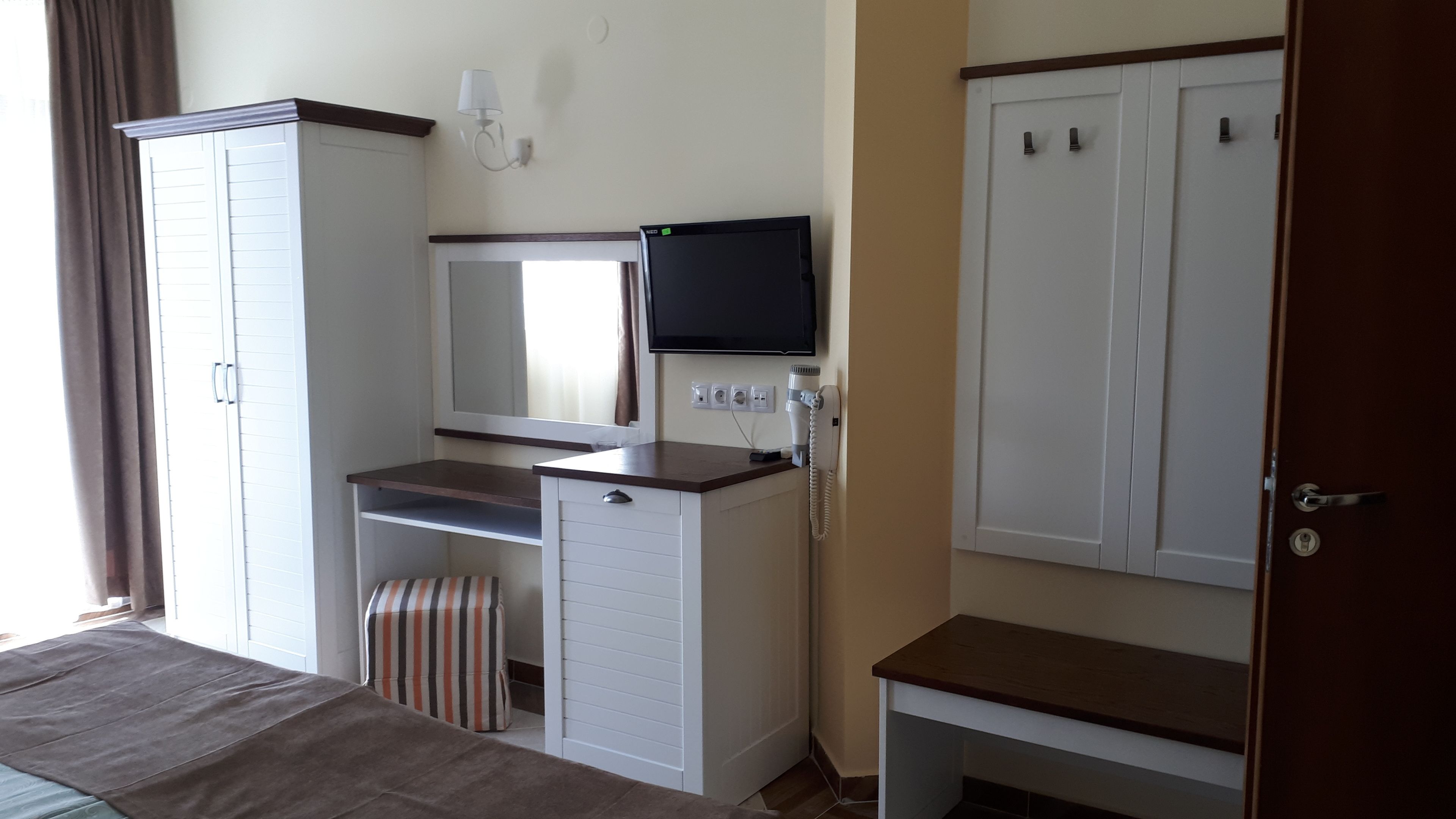 Ein Hotelzimmer mit Bett, Schreibtisch mit Computer und Flachbildfernseher, Kleiderschrank und einer Badezimmertür.