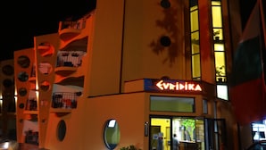 Ein Gebäude mit einzigartigem architektonischen Design, das kreisförmige Öffnungen und Balkone aufweist. Auf der Fassade ist der Name 'EVRIDIKA' sichtbar.