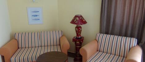 A room with two striped sofas, a small round table, a red lamp, an air conditioning unit, and a framed picture on the wall.