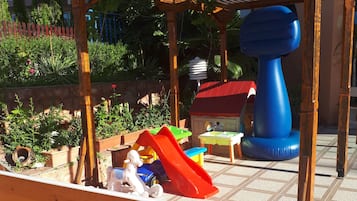 Children can play safely in this outdoor play area featuring a slide, play structure, and toys.