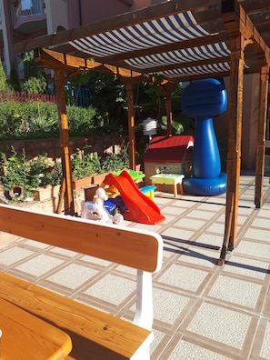 Un banco de madera, un parque infantil con un tobogán y una fuente azul.