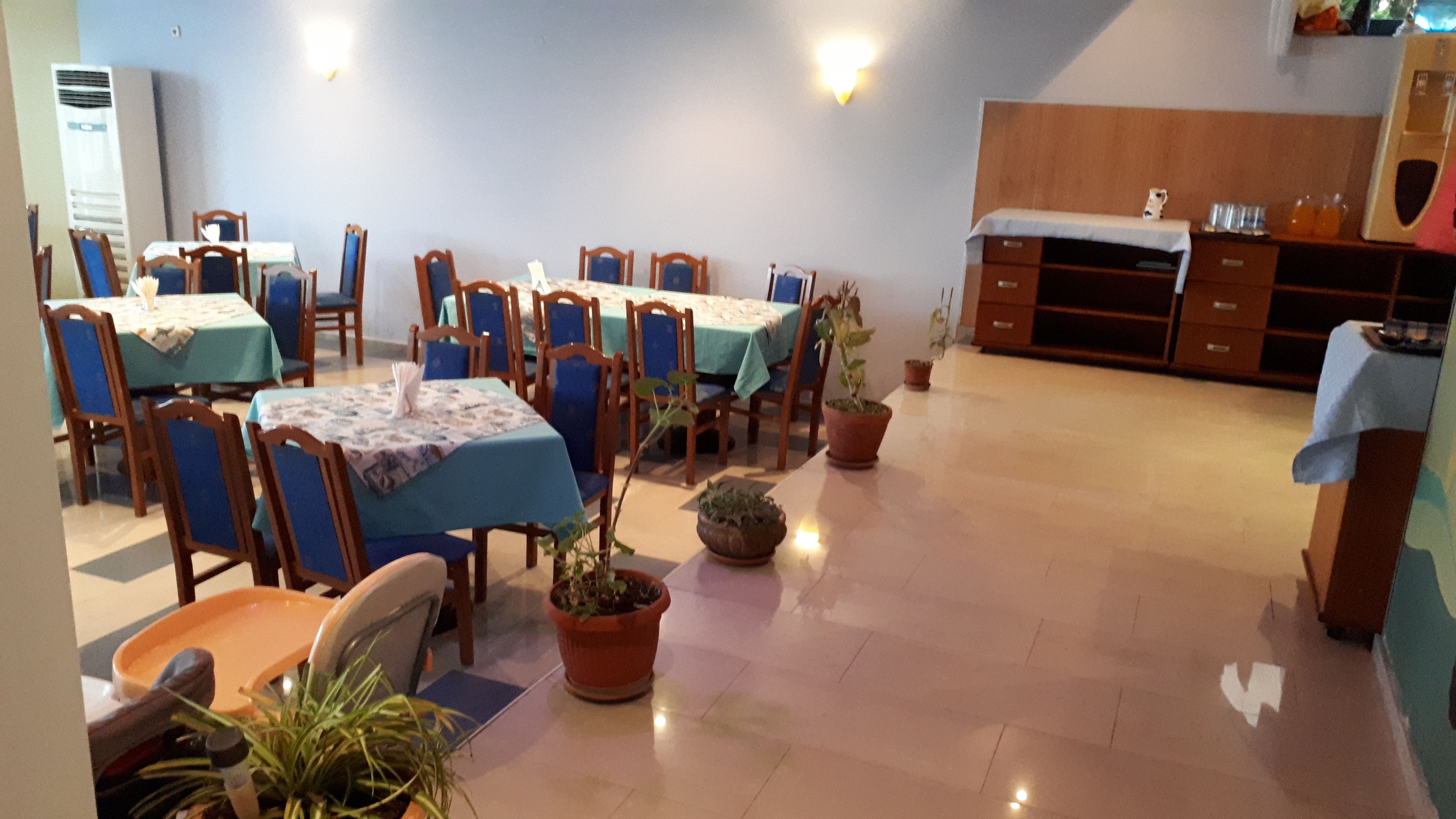 A dining area with tables and chairs, potted plants, and a wooden cabinet.