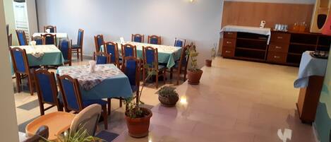 A dining area with tables and chairs, potted plants, and a wooden cabinet.