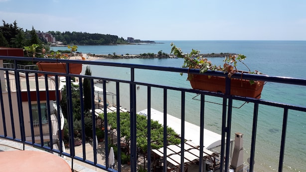 Ein Balkon mit Blumentöpfen, Blick aufs Meer und eine entfernte Küstenlinie mit Gebäuden.
