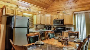 A wooden cabin kitchen with a refrigerator, microwave, stove, and dining table set for four. - Jake's Hideaway (ellijay)
